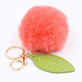 Close-up of fluffy coral pink faux rabbit fur ball keychain with green leaf charm and gold hardware - Orange Red