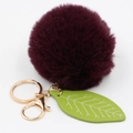 Detailed close-up of a burgundy faux fur pompom keychain with a green leaf accessory - Purplish Red