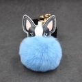 Detail eines blauen Pelz-Bommel-Anhängers mit schwarzem Lederhund und goldener Metallschließe - 8cm / Hellblau