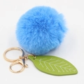 Detailed view of plush blue fur ball keychain with green leaf charm and gold hardware - Light Blue