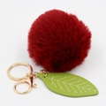 Macro detail of red faux fur pompom keychain with green leaf and golden metal hardware - Burgundy