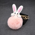 Detailed macro of pink plush bunny ear keychain with fluffy pompom and golden metal clasp - Pink