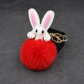Close-up of red fluffy fur pompom rabbit keychain with gold lobster clasp on gray surface - Red