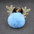 Close-up of fluffy blue plush reindeer keychain with golden glitter antlers on dark base - 8cm Pompom / Light Blue