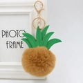 Detail view of pineapple keychain with green leather leaves and soft brown fur pompom - 8cm / Coffee