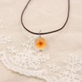Macro d'un pendentif transparent fait main avec fleurs séchées orange et cordon brun - Orange