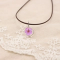 Gros plan détaillé d'un pendentif en résine fait main avec une fleur séchée violette réelle - Violet