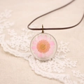 Gros plan d'un pendentif fait main marguerite rose séchée sur une cordelette brune - Série de Fleurs Pressées Réelles / Rose