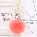 Close-up of fluffy coral pink pompom keychain with golden clasp and unicorn detail - Orange Red