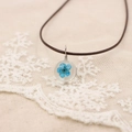 Gros plan d'un collier artisanal avec pétale de fleur séchée bleue en pendentif - Bleu Saphir