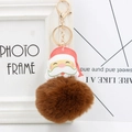 Close-up of fluffy brown pompom keychain with Santa Claus leather charm and gold hook - Brown