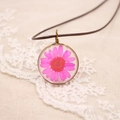 Gros plan d'une marguerite séchée dans un pendentif en résine avec cadre en bronze - Série de Fleurs Pressées Réelles / Rose rouge