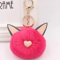 Gros plan d'un porte-clés pompon chat rose vif avec détails dorés et nez en forme de cœur - Style Chaîne De Clé Or / Rouge Rose