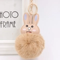 Close-up of cute rabbit faux fur keychain with light brown plush ball and golden ring clip - Khaki