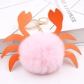 Gros plan d'un porte-clés crabe en pompon rose avec pinces en similicuir orange et anneau doré - Rose Clair