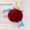Detailed macro shot of red plush pompom and blue faux leather dolphin charm with gold clasp - Burgundy
