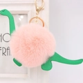 Nahaufnahme des rosa Plüsch-Dinosaurier-Schlüsselanhängers mit grünem Leder und Goldclip - Dinosaurier-Stil / Rosa