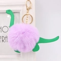 Close-up of green leather dinosaur keychain with purple fluffy fur pompom and gold clip - Dinosaur Style / Taro Purple