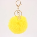 Detail of a bright yellow faux fur ball keychain with gold hardware and a 3D cube charm - Yellow
