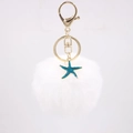 Close-up of white fluffy pompom keychain with golden metal clasp and blue starfish charm - White