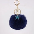 Close-up of fluffy dark blue pompom keychain with golden clasp and starfish charm - Navy Blue