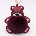 Gros plan du porte-clés ours en cuir bordeaux avec pompon violet et anneau doré - Style Chaîne De Clé Or / Rouge Pourpre & Rouge