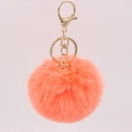 Close-up of fluffy coral faux fur keychain with gold lobster clasp and metal geometric charm - Orange Red
