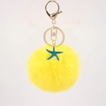 Macro detail of a yellow pompom keychain with a blue starfish charm and gold lobster clasp - Yellow