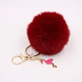 Macro detail of fluffy red faux fur pompom with golden keychain and pink flamingo pendant - Burgundy