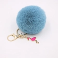 Close-up of blue faux fur pompom keychain with golden metal clasp and pink flamingo charm - Teal