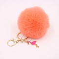 Detail view of a fluffy coral faux fur pompom keychain with a golden flamingo charm - Orange Red