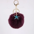 Detail of dark purple faux fur pompom keychain with blue starfish pendant and gold clasp - Purplish Red