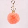 Macro detail of peach faux fur keychain with golden shell pendant and white pearl - Orange Red