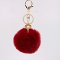 Detailed macro view of a red fluffy pompom keychain with golden shell and pearl charm - Burgundy