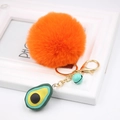 Close-up of orange faux fur pompom keychain with avocado charm and golden lobster clasp - Avocado Keychain / Orange