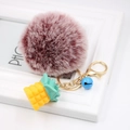 Close-up of fluffy faux fur pompom keychain with yellow pineapple and blue bell charm - Dual-color Red