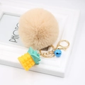 Detail of a beige faux fur pompom keychain with golden pineapple charm and blue bell - Nude