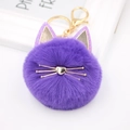 Close-up of a purple plush cat ball keychain with golden whiskers and heart-shaped nose - Deep purple