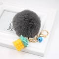 Detail of grey fluffy pompom keychain with yellow pineapple charm and a blue bell - Dark Gray