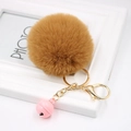 Detailed macro view of a fluffy faux fur pompom keychain with golden metal clasp and pink bell - Coffee