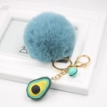 Detail of greyish blue faux fur pompom keychain with golden lobster clasp and avocado charm - Avocado Keychain / Teal