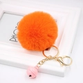 Detailed close-up of a bright orange fluffy pompom keychain with a pink bell and gold clasp - Orange