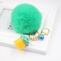 Close-up of mint green faux rabbit fur pompom keychain with golden pineapple charm and blue bell - Grass Green