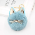 Close-up of light blue plush cat keychain with golden ears and metal whiskers - Teal