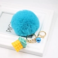 Close-up of a blue faux fur pompom keychain with a pineapple charm and a small bell - Lake Blue