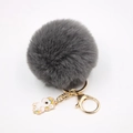 Gros plan du porte-clés pompon gris avec fermoir doré et pendentif licorne - Porte-clés Licorne / Gris Foncé