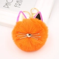 Detailed close-up of an orange cat pompom keychain with gold-tone cat ears and whiskers - Orange