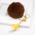 Detail view of brown faux fur pom pom keychain with a yellow banana charm and golden clasp - Brown