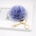 Macro detail of purple faux fur pompom keychain with gold lobster clasp and white pearl charm - Double Blue