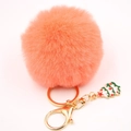 Détail d'un porte-clés pompon en fausse fourrure rose-orangé avec pendentif sapin de Noël - Rouge Orangé